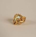 An asymmetric oblong opal encrusted in a gold band with an ornate plant motif
