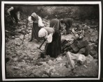 Three women and two men in traditional costume bent over a pile of rubble with pick-axes