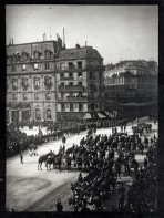 Paris street (seen from above) lined with onlookers dressed in black and a procession of horses