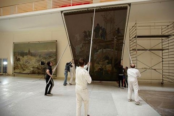 The Slav Epic arrives in Prague Several men hoist up one of the Slav Epic canvases using a metal structure and metal poles