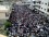 A demonstration in the city of Banyas, Syria A street filled with protestors with white buildings on either side seen from above